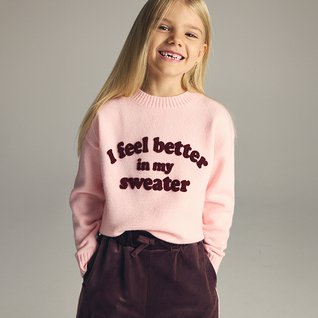 A child wearing a white long-sleeve top with text "Find the magic" and a sparkling light blue tutu-style skirt. The pose suggests a sense of wonder or joy. The background is plain and light for a clean presentation.