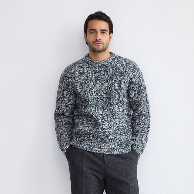 A person sits casually on a stool placed on a patterned rug in a minimalist room. Bright natural light streams through two large windows behind them, creating a serene atmosphere. The pose and setting suggest a relaxed moment indoors. banner