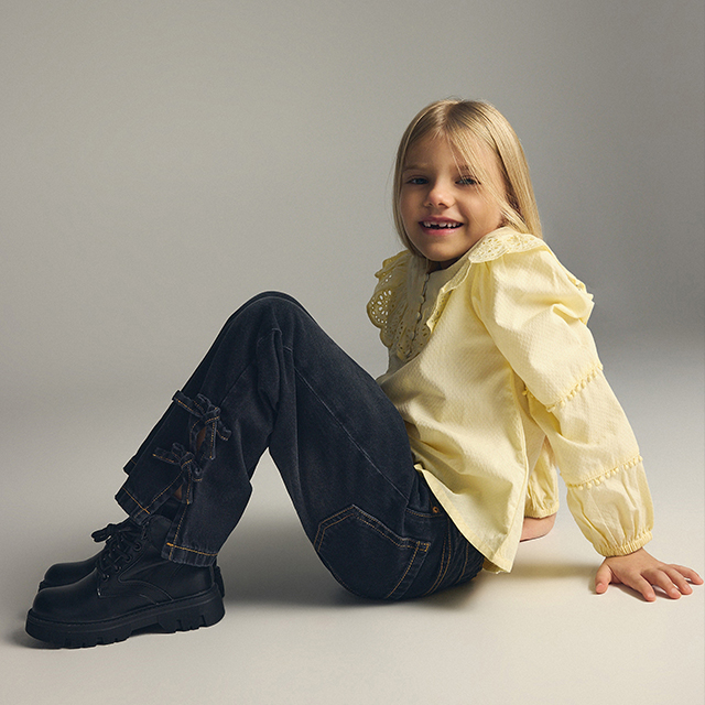 A child wearing a white long-sleeve top with text "Find the magic" and a sparkling light blue tutu-style skirt. The pose suggests a sense of wonder or joy. The background is plain and light for a clean presentation.