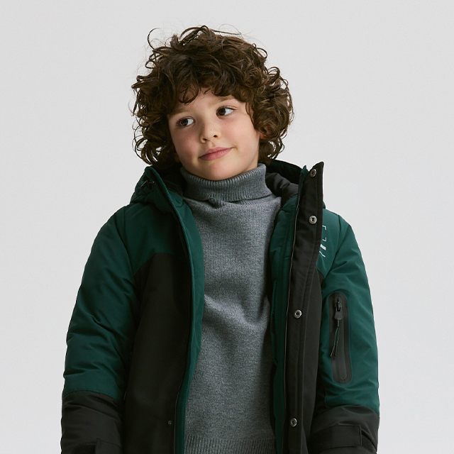 Two children are sitting on connected black chairs, wearing casual outfits with jeans, white hoodies, and green sneakers. Both are holding something in their hands and pointing forward, possibly pretending to aim or gesture. Their actions suggest playfulness or engagement in a game. banner