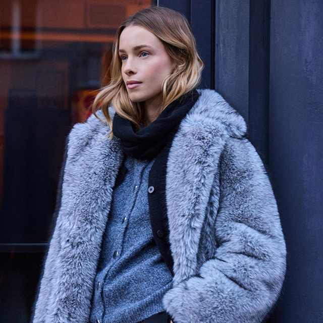 A person wearing a dark suit and tie sits with arms crossed against a plain background. banner